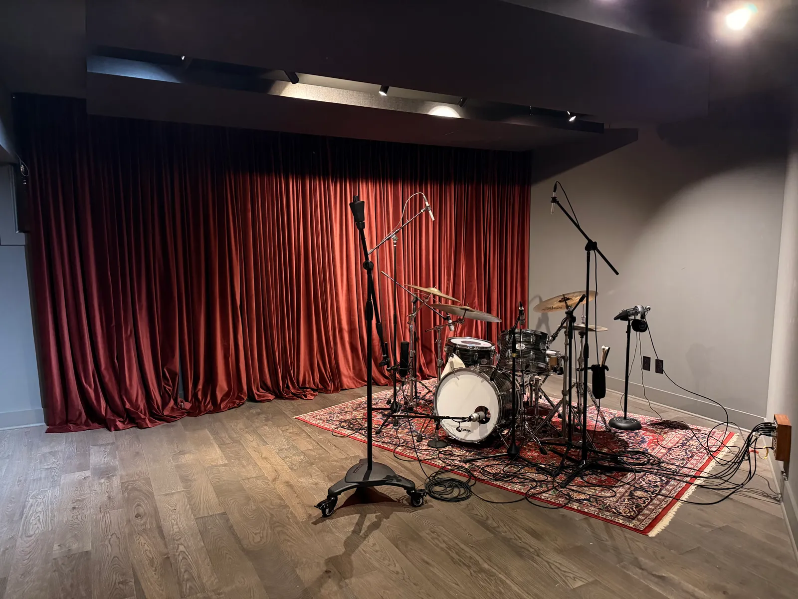 Live room with the drum kit set up, curtains drawn behind, clouds overhead. Tie line panel on the right wall.